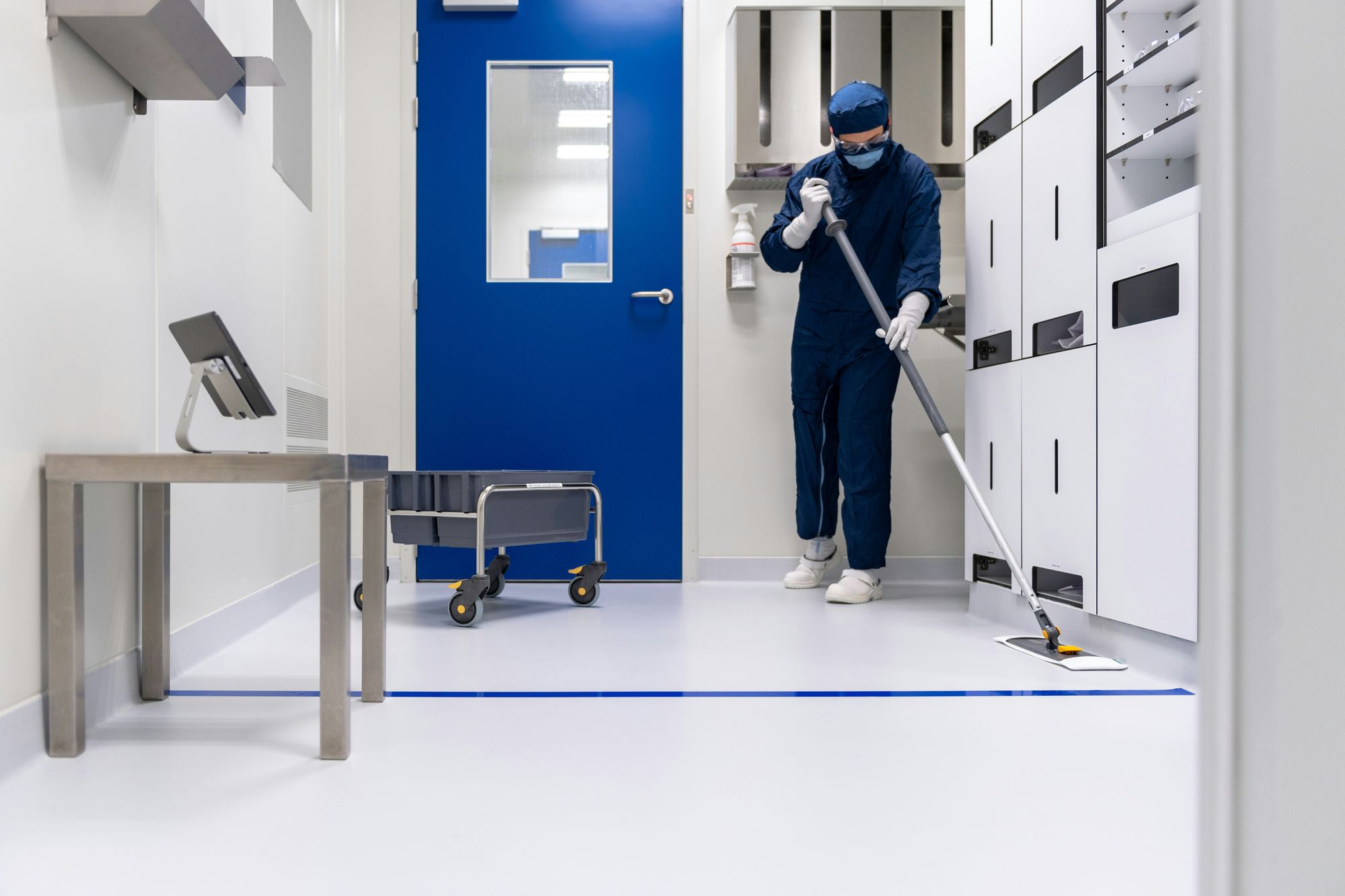 Cleaner mopping a spotless corridor beside a blue door