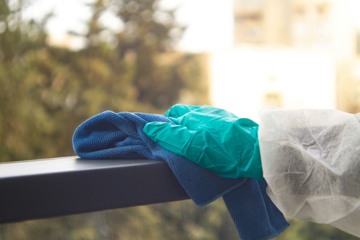 Gloved hand wiping down a handrail with a cloth